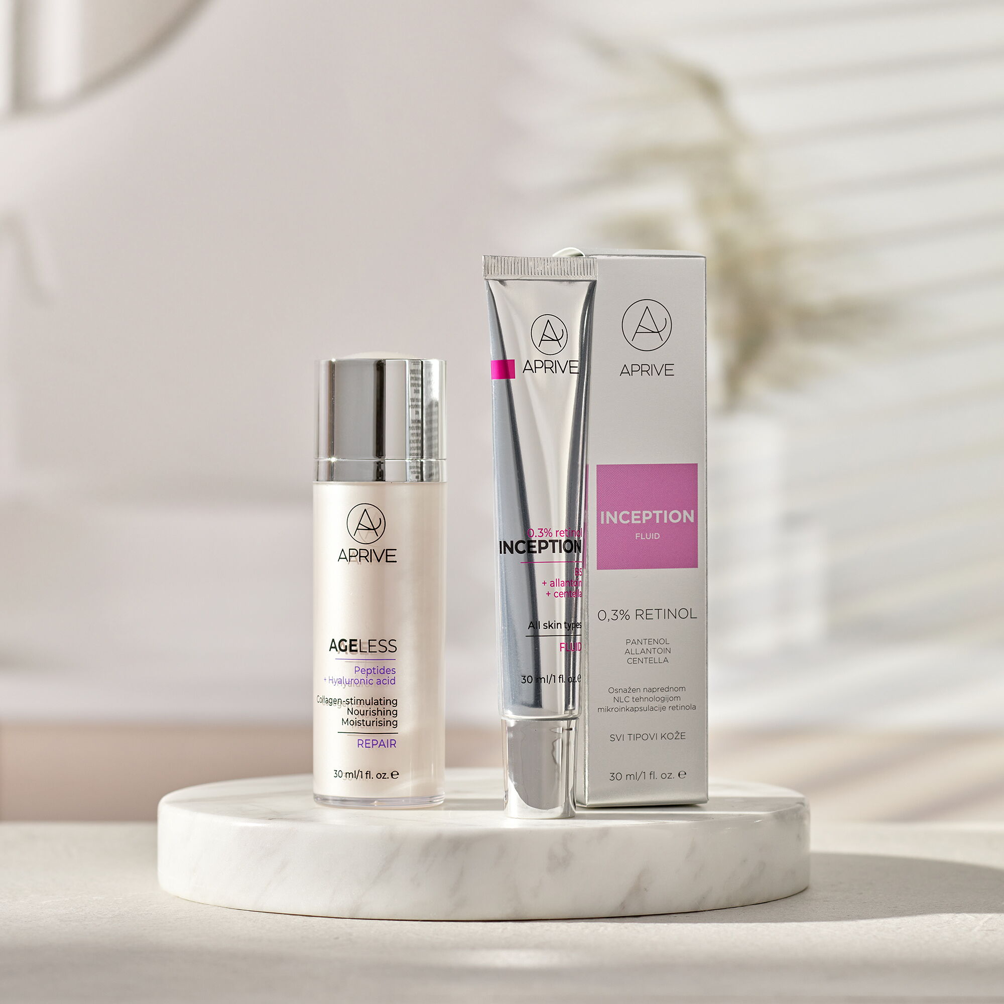 Aprive Inception 0,3% Retinol fluid tuba s kutijom i Ageless Peptides + Hyaluronic Acid Repair serum bočica izloženi na bijelom mramornom postolju.