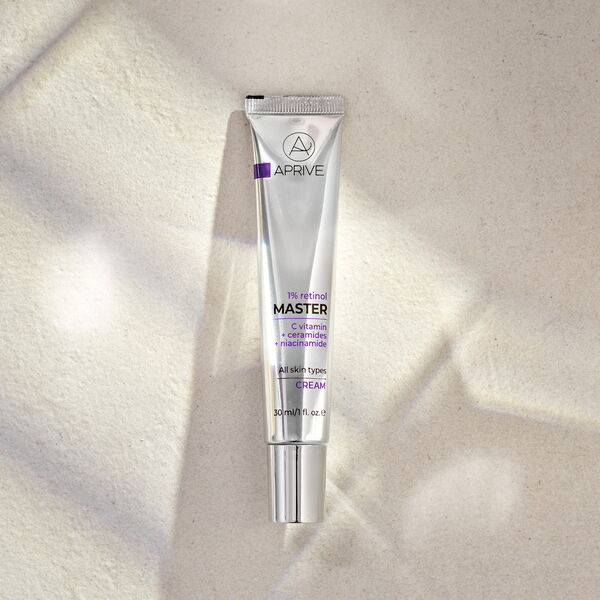 Silver tube of Aprive 1% Retinol Master Cream, containing Vitamin C, ceramides, and niacinamide, on a textured beige background with soft shadows.