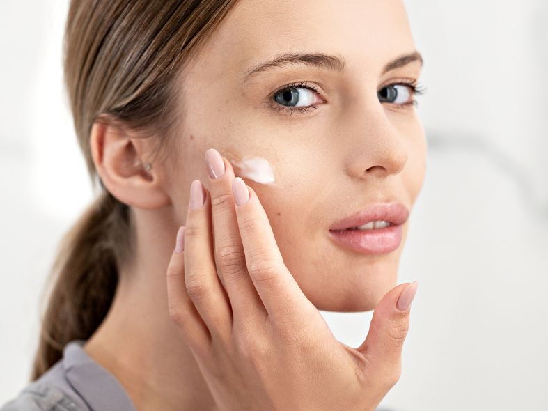 A woman with clear skin gently applying a white retinol face cream to her cheek.
