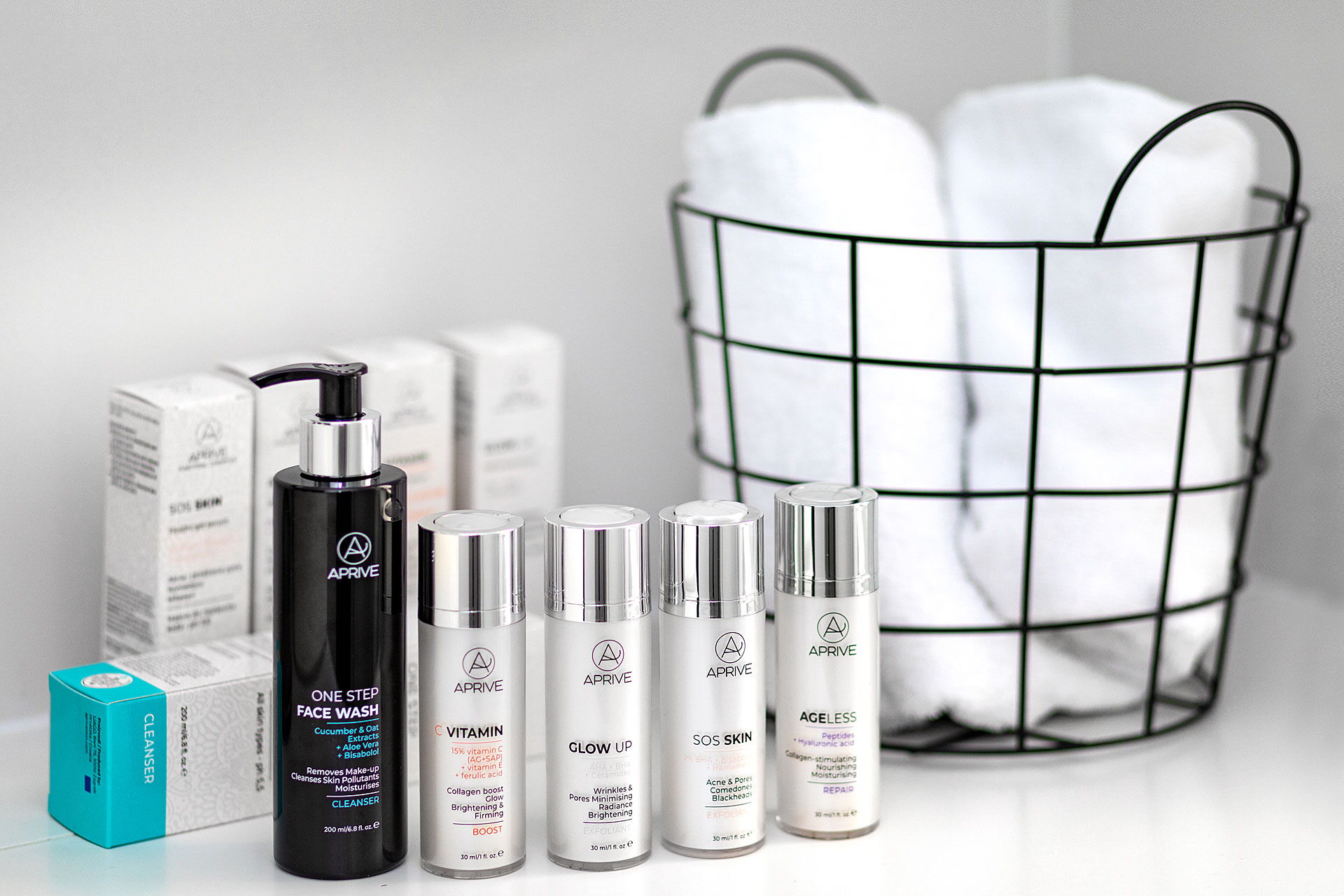 Collection of Aprive cosmeceutical skincare products including cleanser and various serums arranged next to white towels in a wire basket.