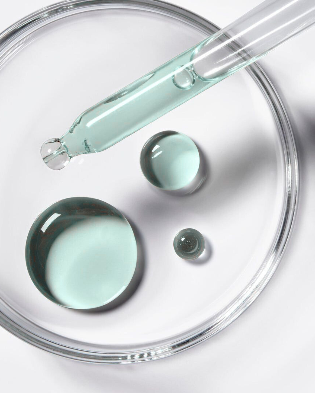 Close-up view of a glass dropper dispensing liquid drops of ferulic acid ingredient serum into a laboratory petri dish.