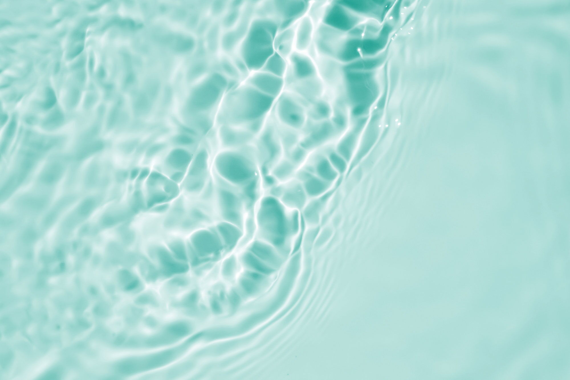 Top-down view of turquoise water surface with sunlight rippling and creating patterns, suitable as a fresh background.