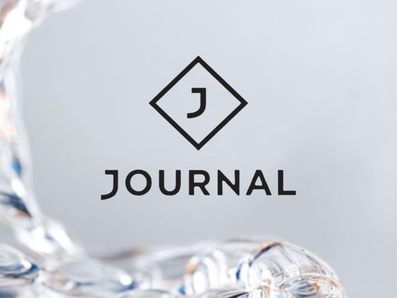Black 'J' letter inside a diamond shape logo, with 'JOURNAL' text below, set against a blurred abstract background of splashing clear liquid.