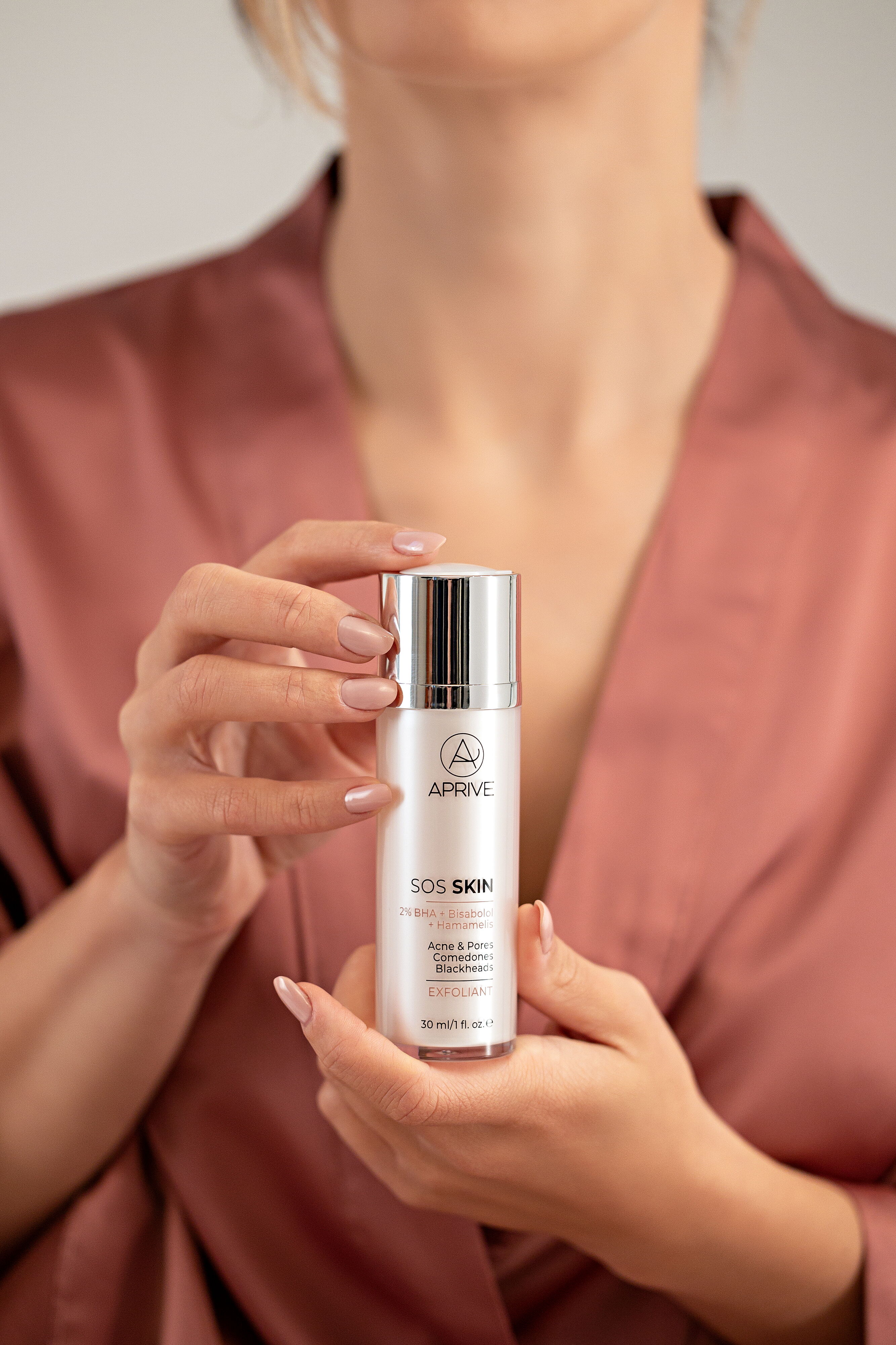 Close-up of a woman holding the APRIVE SOS Skin Exfoliant serum bottle, detailing ingredients 2% BHA, Bisabolol, and Hamamelis for acne and pore treatment.