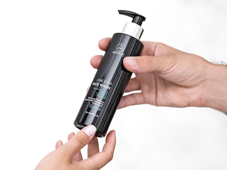 A person's hands holding a black pump bottle of Aprive One Step Face Wash cleanser.