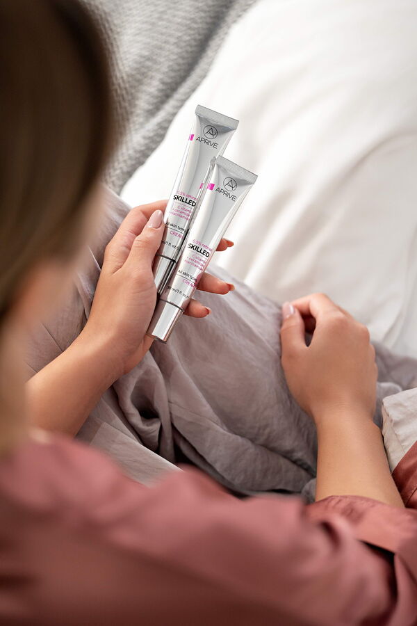 Woman holding two tubes of Aprive SKILLED 0.5% retinol cream enriched with Vitamin C, ceramides, and niacinamide.