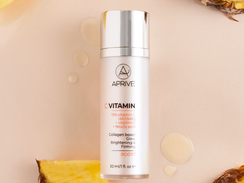 APRIVE C Vitamin Boost serum bottle containing 15% vitamin C, vitamin E, and ferulic acid, surrounded by serum drops and pineapple slices.