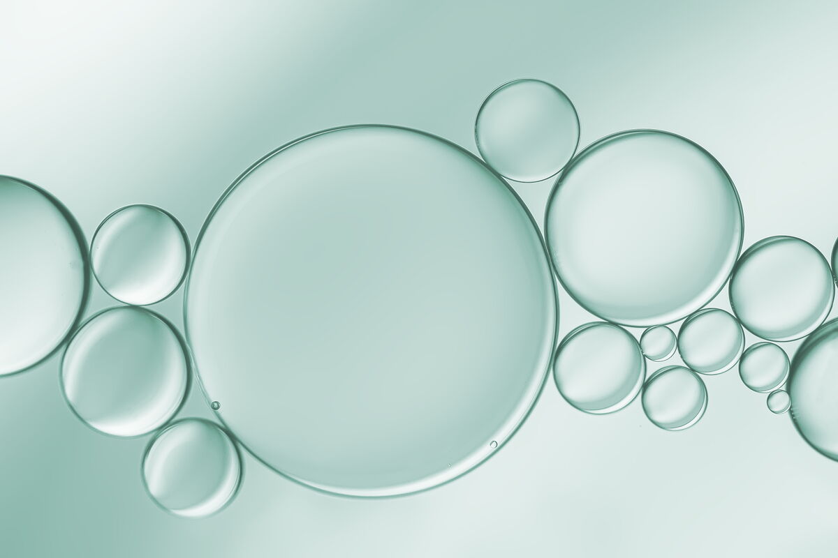 Close-up view of clear oil bubbles of various sizes floating in a light green liquid, representing a cosmetic skincare ingredient.
