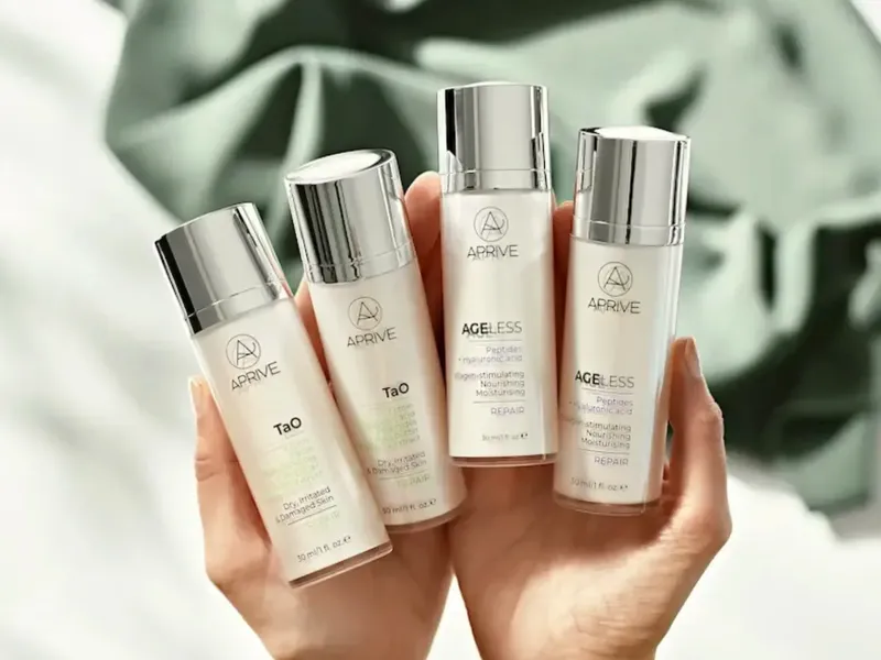 A hand holding four APRIVE skincare bottles, including TAO and AGELESS lines with peptides and hyaluronic acid for skin repair.