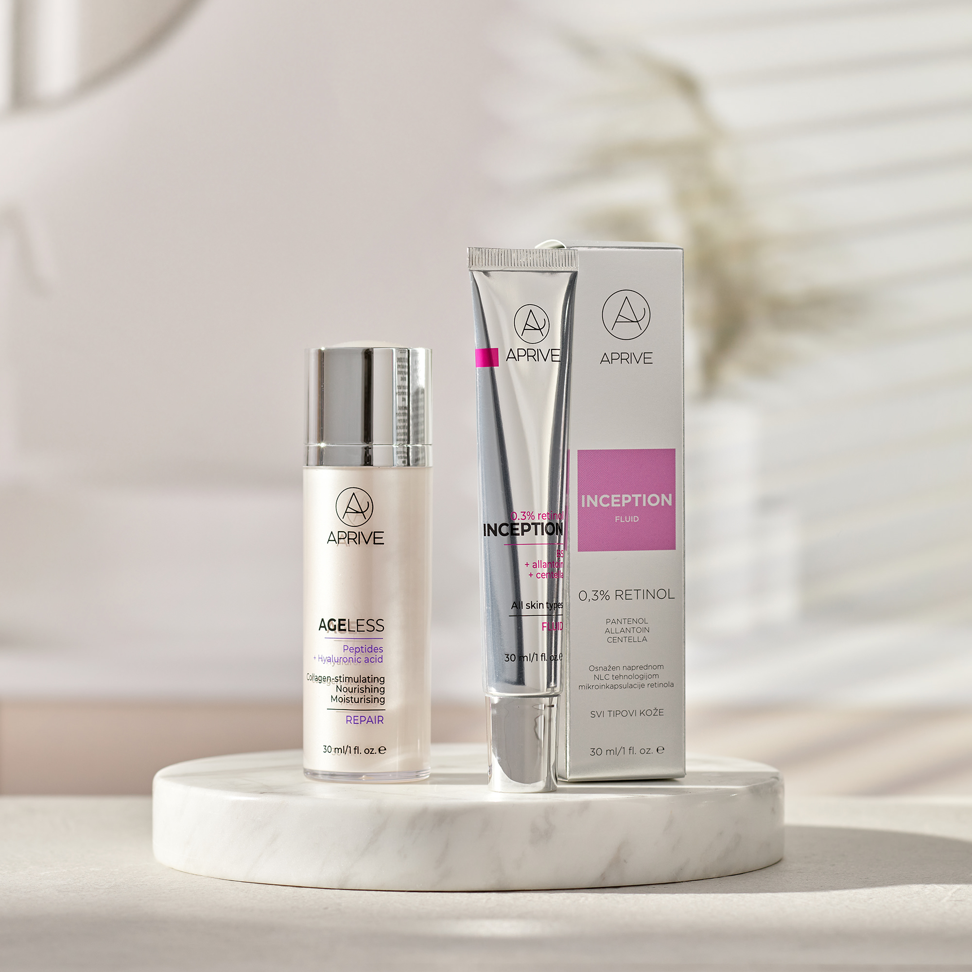 Aprive Inception 0,3% Retinol fluid tuba s kutijom i Ageless Peptides + Hyaluronic Acid Repair serum bočica izloženi na bijelom mramornom postolju.